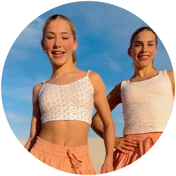 Woman wearing a white halter vest and jeans. She is holding an iced coffee and sunglasses.