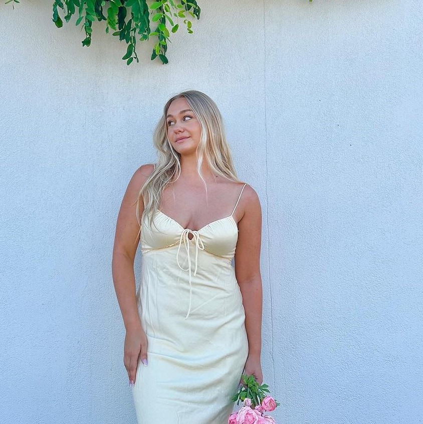 Woman wearing a white silk dress holding flowers and posing
