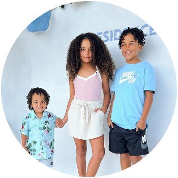 Brunette woman wearing a green crop top and white skirt, posing in front of a greenery wall